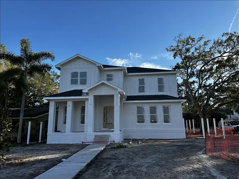 Freshly painted white two-story home exterior with trim and porch, framed by oak trees