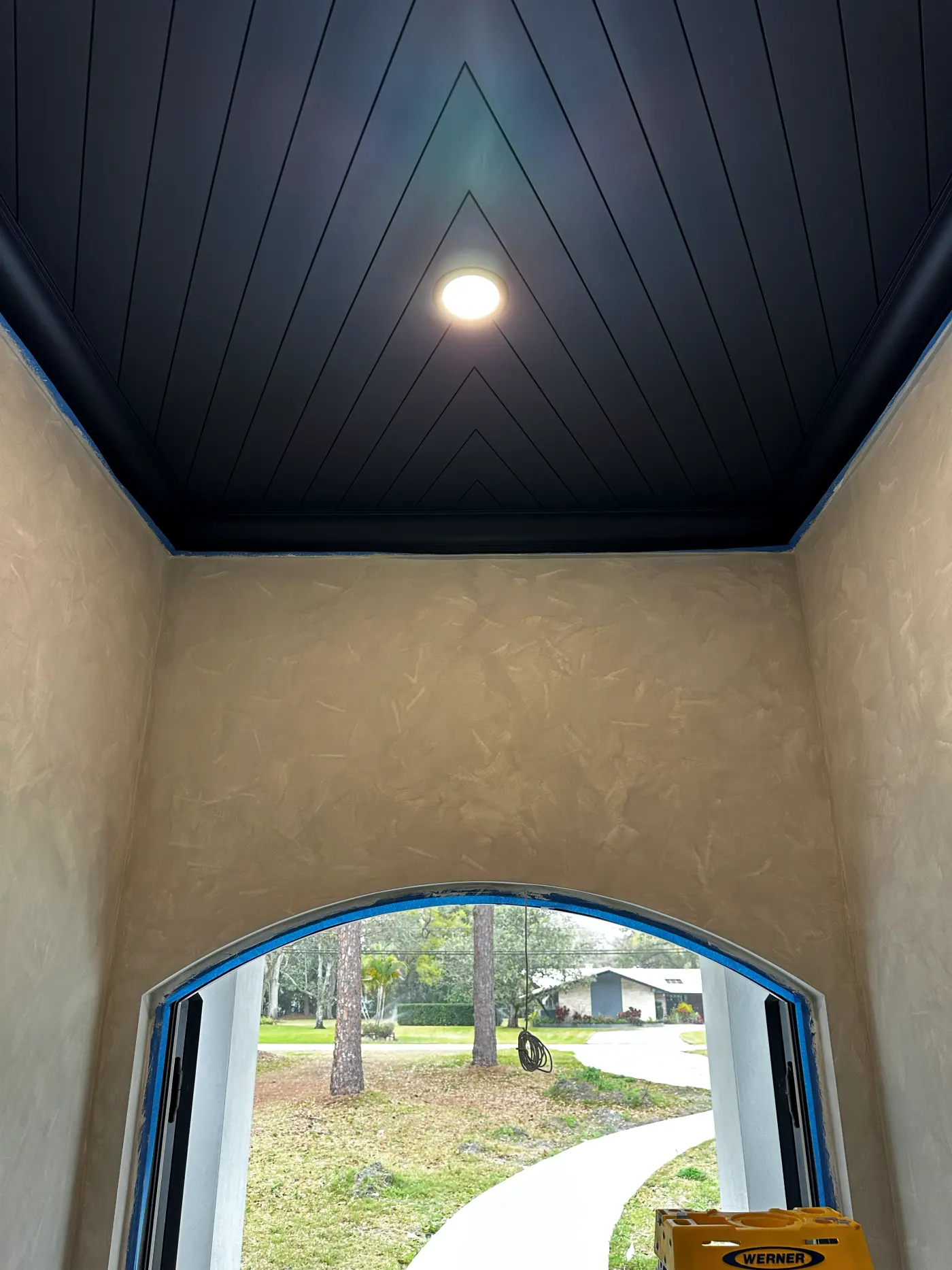 Hallway with limewash walls, a dark shiplap ceiling and an arched window at the end