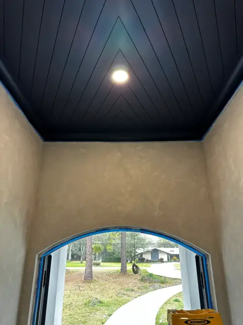 Hallway with limewash walls, a dark shiplap ceiling and an arched window at the end