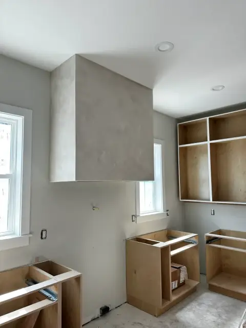 Custom range hood surround finished in textured limewash beside unfinished cabinet boxes