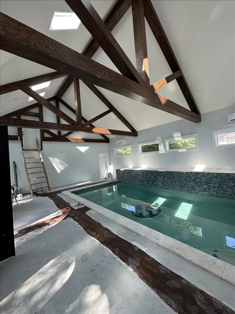 Stained dark wood roof trusses above an indoor pool room with white walls
