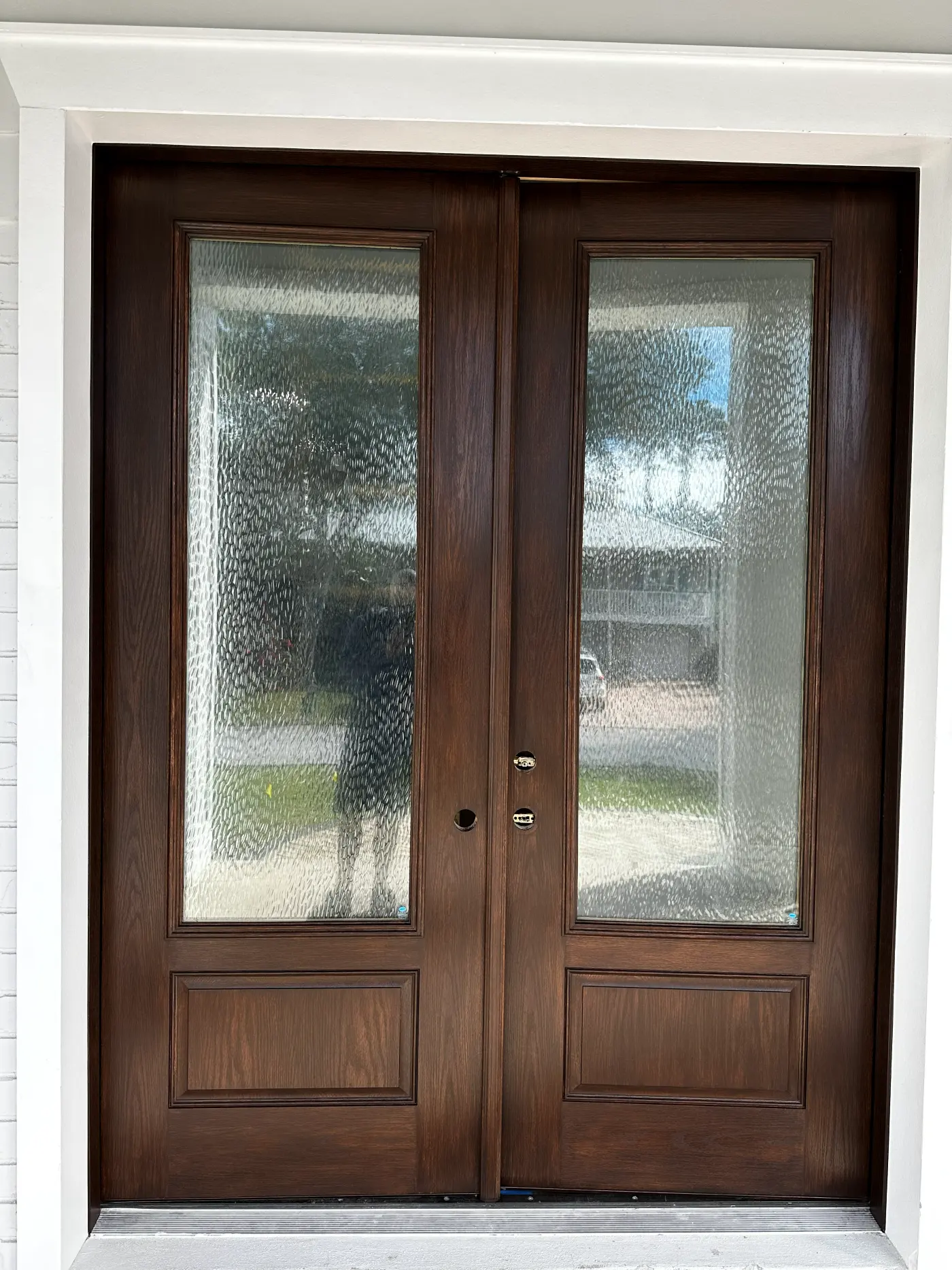 Stained wood double entry doors with frosted glass panels and white trim