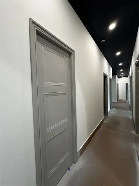 Gray painted paneled door and trim in a long hallway with a black ceiling