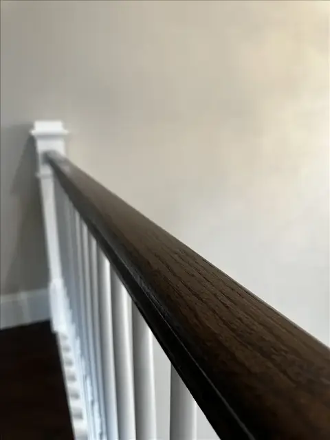 Dark stained stair handrail with crisp white balusters and smooth painted wall